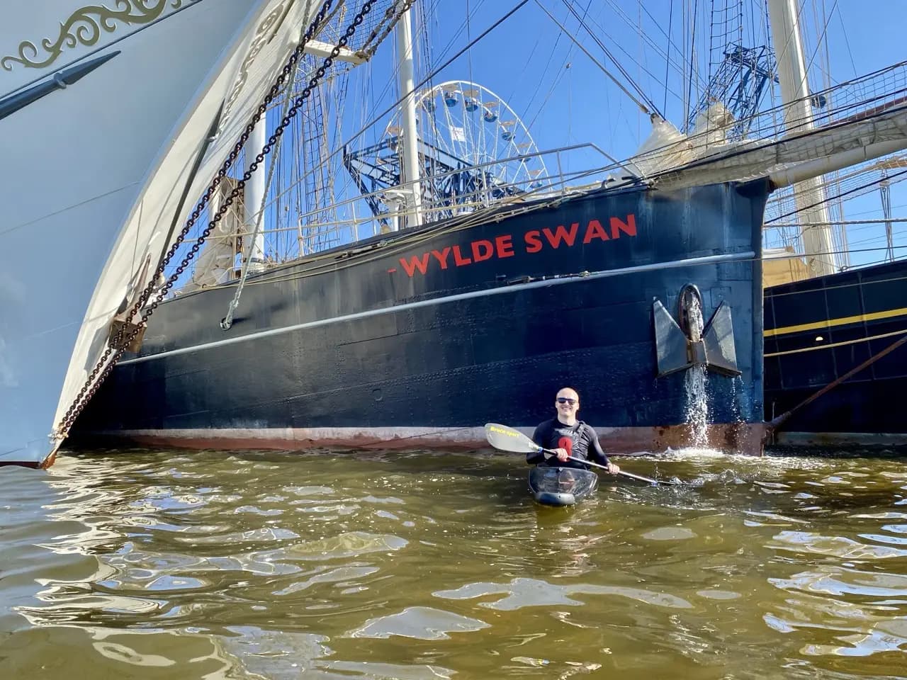 Jan paddling a kayak past the tall ship Wylde Swan